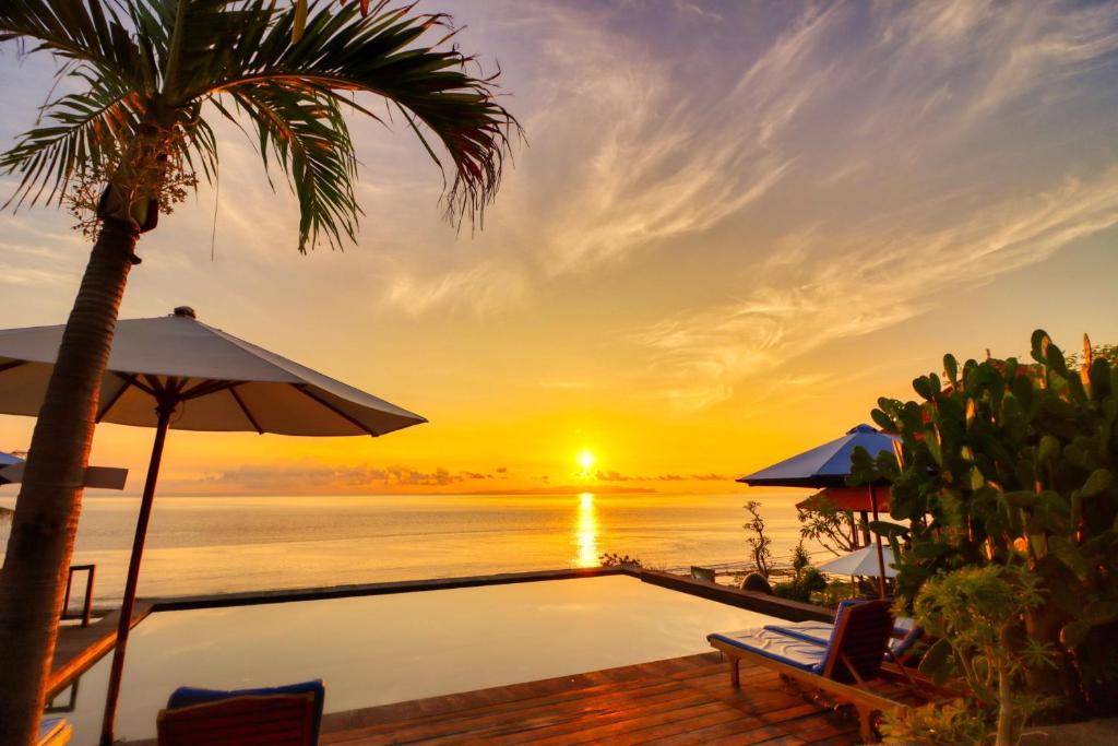 a pool with a palm tree and a sunset at Manta Cottage Seaview Plus in Nusa Penida