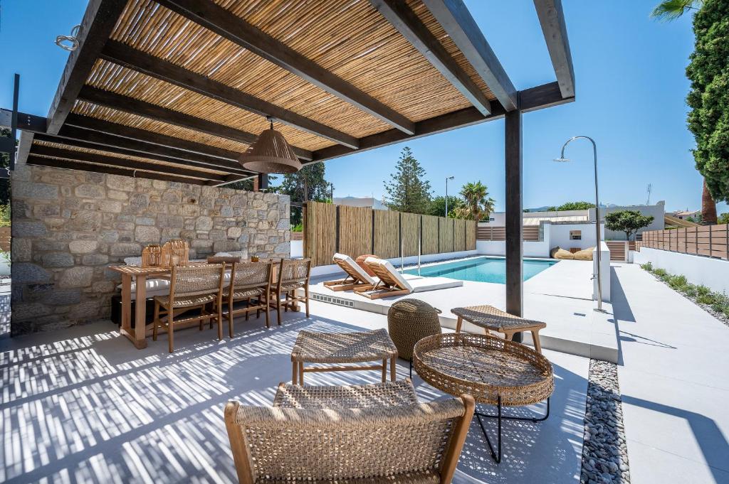 eine Terrasse mit einem Tisch, Stühlen und einem Pool in der Unterkunft RASTONI VILLAS BY AEGEAN HOUSES in Psalidi