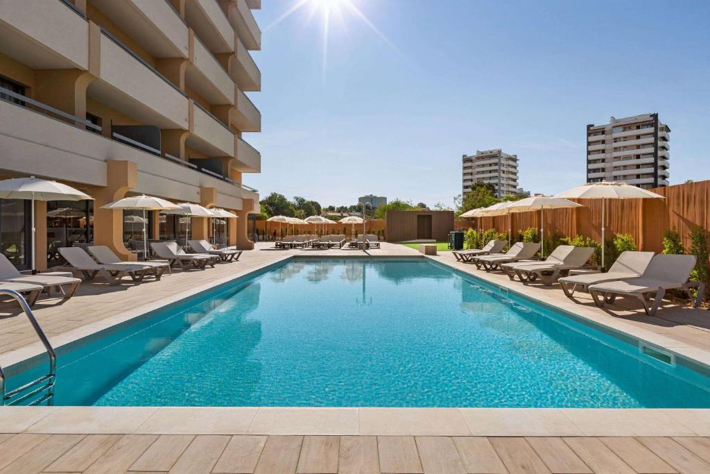 uma piscina com cadeiras e guarda-sóis num hotel em Wyndham Residences Alvor Beach em Alvor