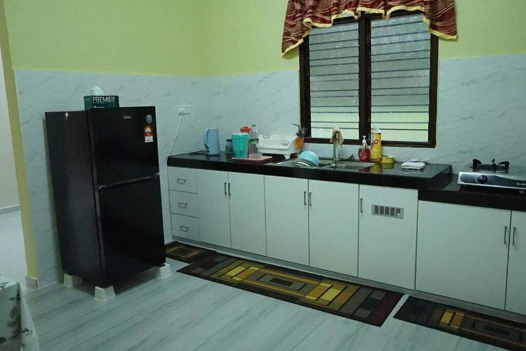 a kitchen with a black refrigerator and white cabinets at ZZ Homestay in Bukit Payong