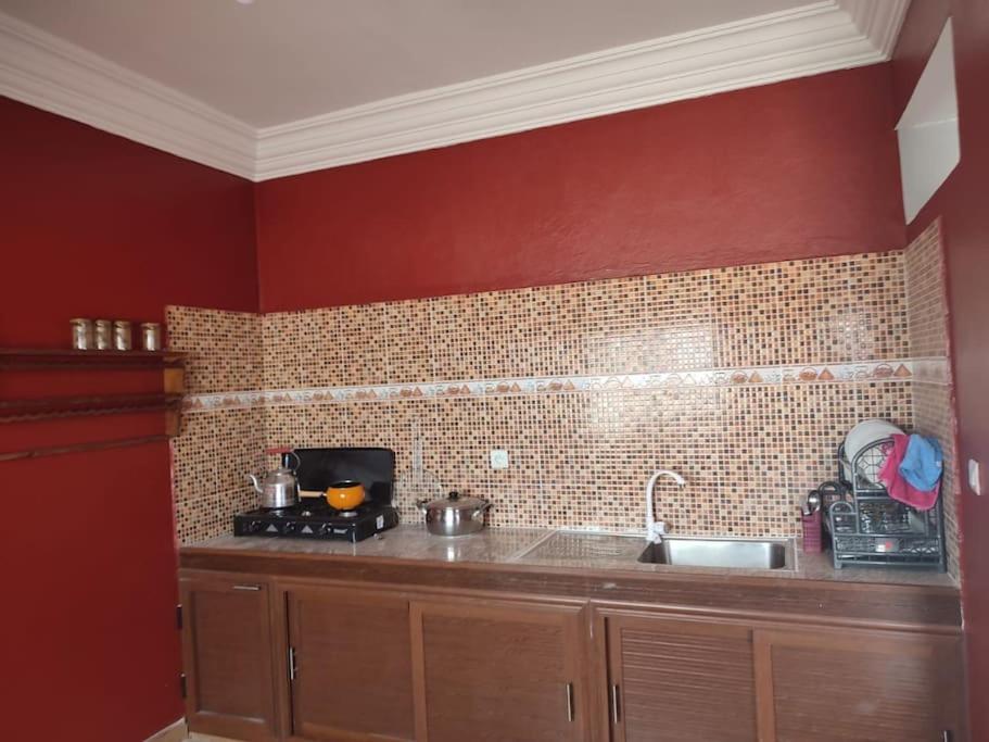 uma cozinha com paredes vermelhas, um fogão e um lavatório em Dar Si Brahim, cozy house in Hyoute chair em Oualidia
