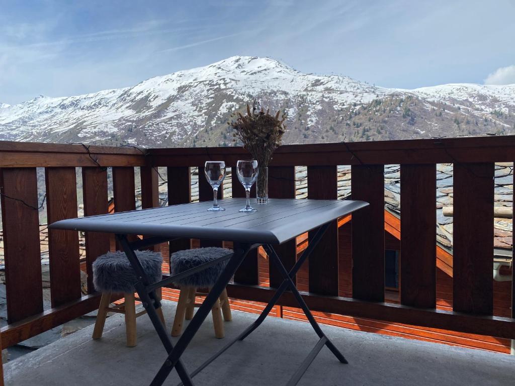 a table with wine glasses on a balcony with a snow covered mountain at Appartement 4-6 personnes à Valmeinier 1800 résa du samedi au samedi avec piscine intérieure chauffée in Valmeinier