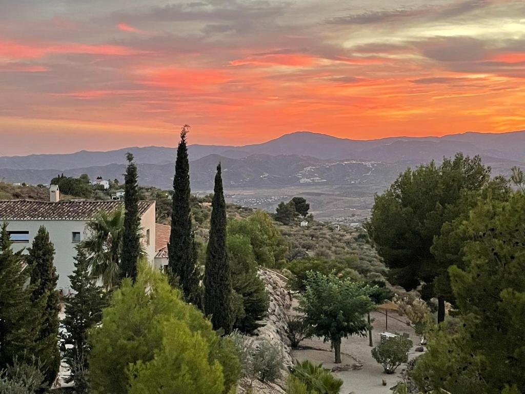 a sunset over the hills with trees and a building at Boutique B&B El Refugio in Alcaucín