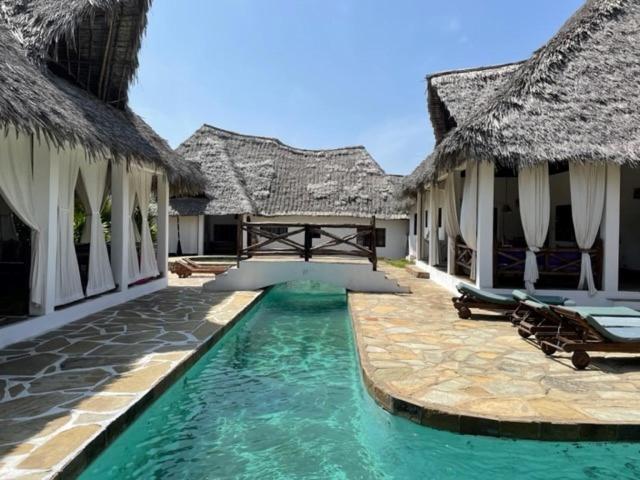 a swimming pool in front of a resort with thatched buildings at Lion Garden Villa 6 in Malindi