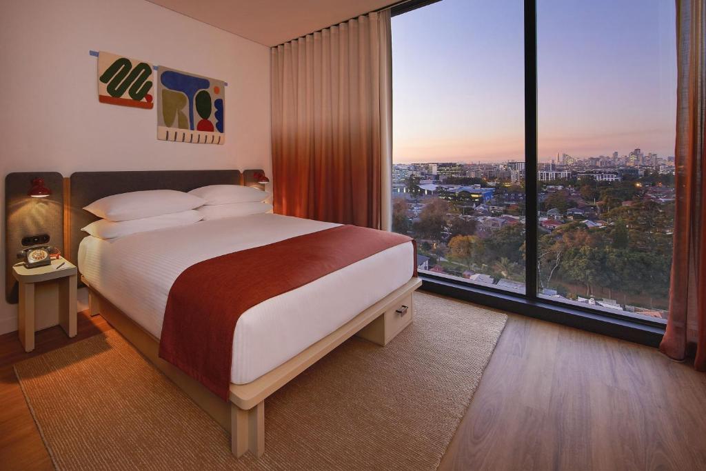 a bedroom with a large bed and large windows at Moxy Sydney Airport in Sydney