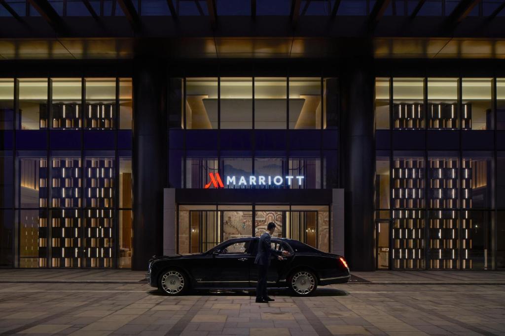 Ein Mann steht neben einem Auto vor einem Marriot-Gebäude. in der Unterkunft Shantou Marriott Hotel in Shantou