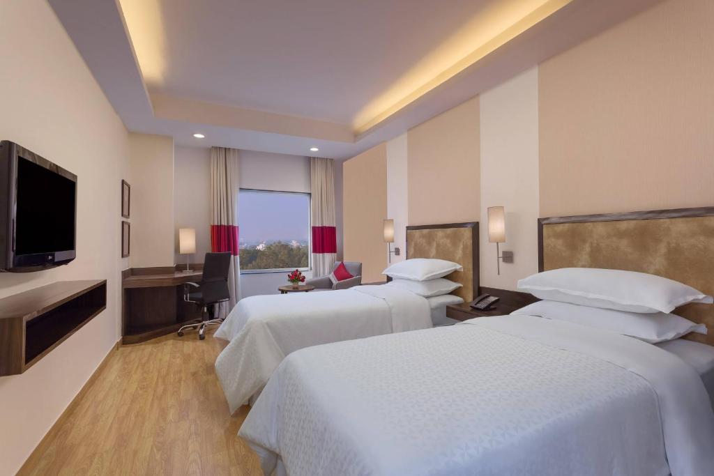 ein Hotelzimmer mit 2 Betten und einem Flachbild-TV in der Unterkunft Four Points by Sheraton Vadodara in Vadodara