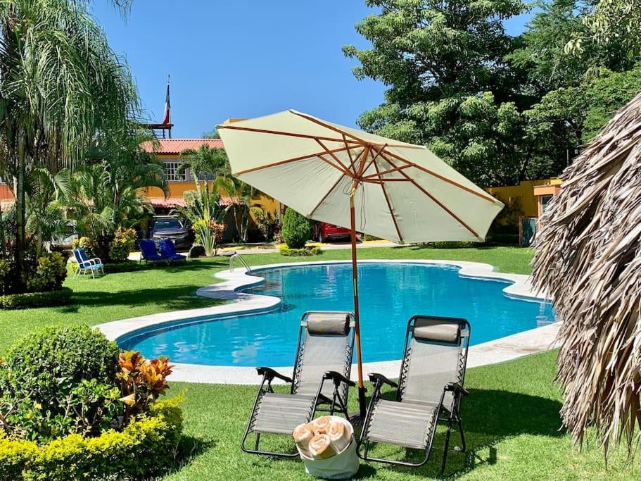 zwei Stühle und ein Regenschirm neben einem Pool in der Unterkunft Acogedora casa en Morelos in Tezoyuca