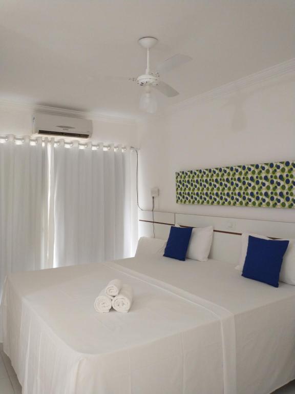 1 dormitorio blanco con 1 cama blanca grande con almohadas azules en Recanto Taperapuan Residencial Mont Carmelo en Porto Seguro