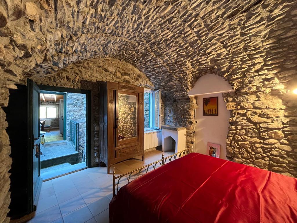 a bedroom with a stone wall and a red bed at Casa Victoria - Full equipped stone house in Rocchetta Nervina