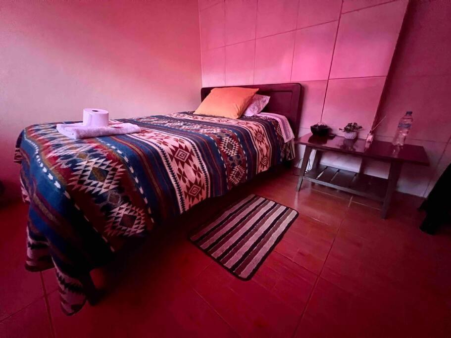 a pink room with a bed and a table at Hermosa habitación con terraza y vista al pastaza in Baños