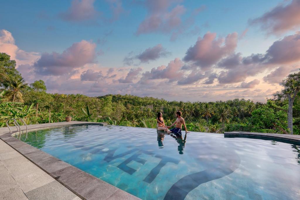 a man and woman sitting on the edge of a swimming pool at Beten Juwet in Nusa Penida