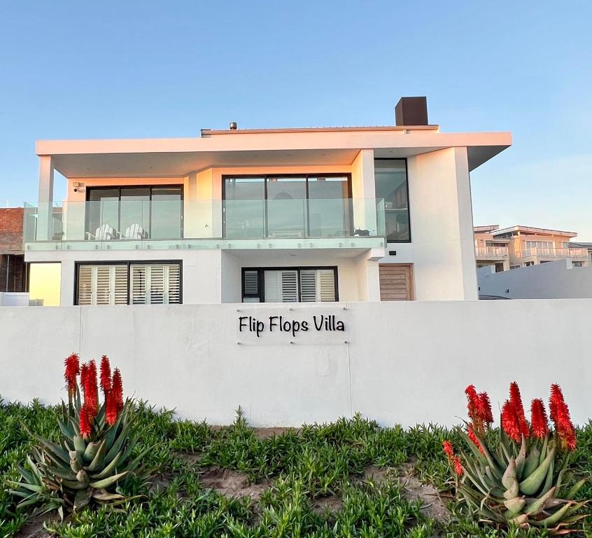 a house with red flowers in front of a wall at Flip Flops Villa in Yzerfontein