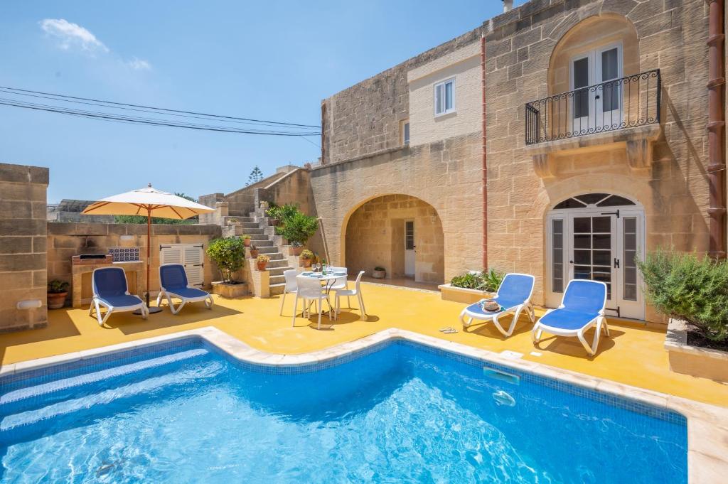 a house with a swimming pool with chairs and an umbrella at Dar ta' Betta Farmhouse with private pool in Għarb
