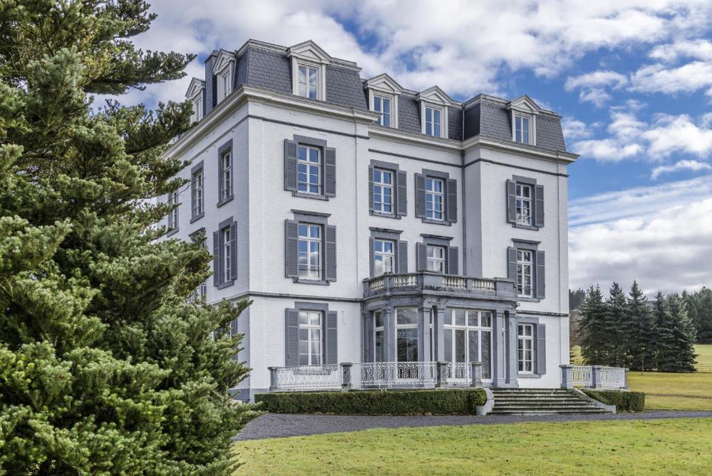 une grande maison blanche avec un arbre dans l'établissement Château Charles, à Pepinster