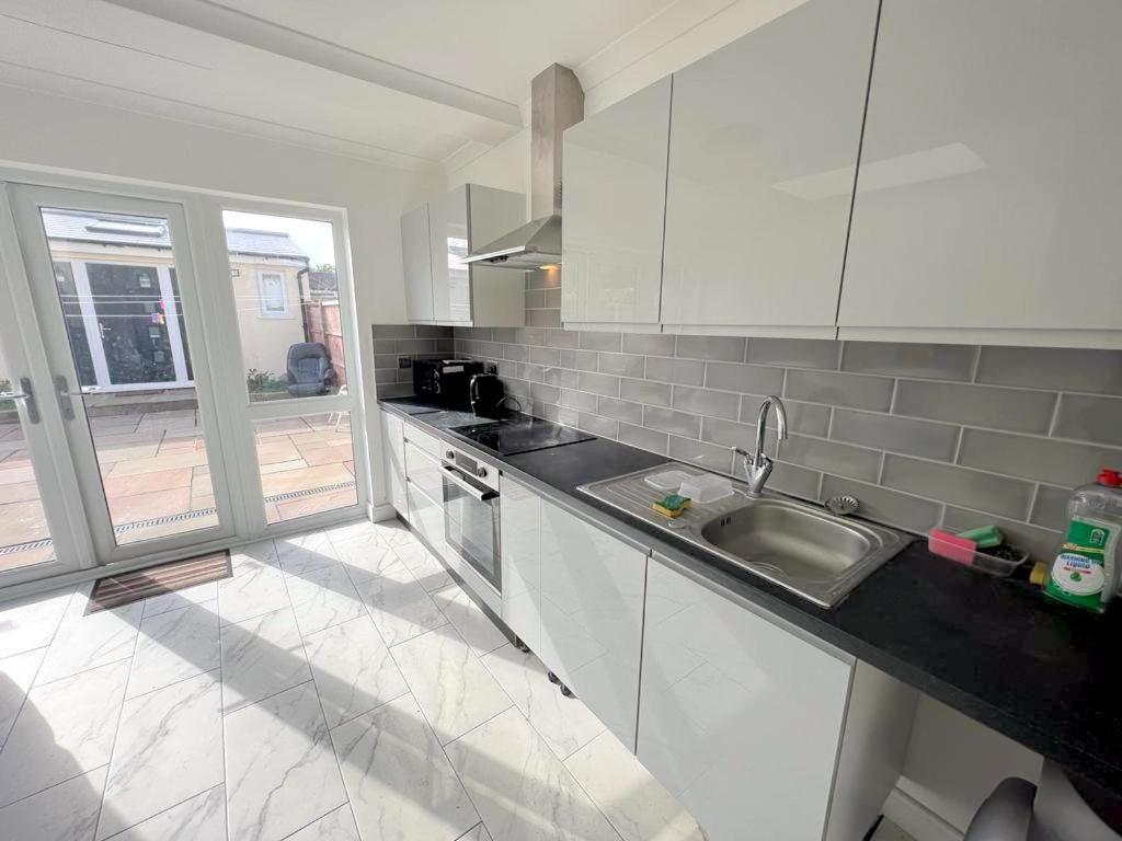 a white kitchen with a sink and a window at Deluxe Ringwood Rooms in Hackbridge