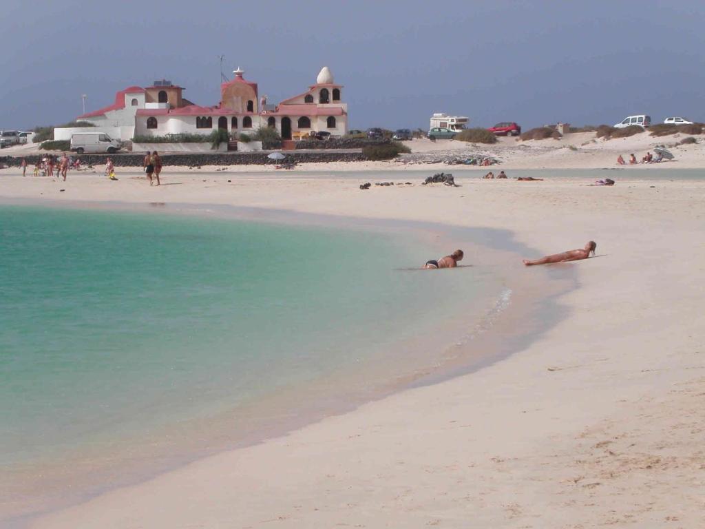 a group of people laying in the water on a beach at El Carmen in El Cotillo