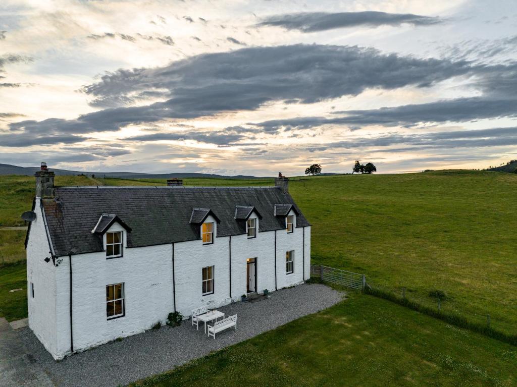 a white house with a bench in a field at Achnahatnich House in Aviemore