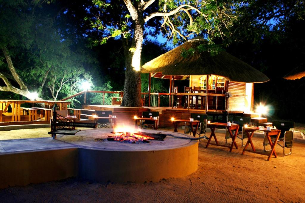 eine Feuerstelle mit Tischen und einem Baum in der Nacht in der Unterkunft Lion Tree Top Lodge in Guernsey Nature Reserve