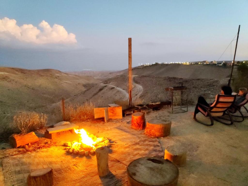 a person sitting in a chair next to a fire at Desert's Edge Eco Tent in Arad