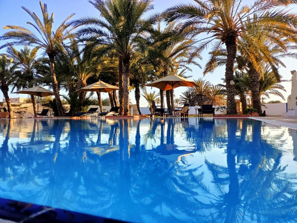 a large swimming pool with palm trees and umbrellas at Le Patio de Mezraya in Mezraya