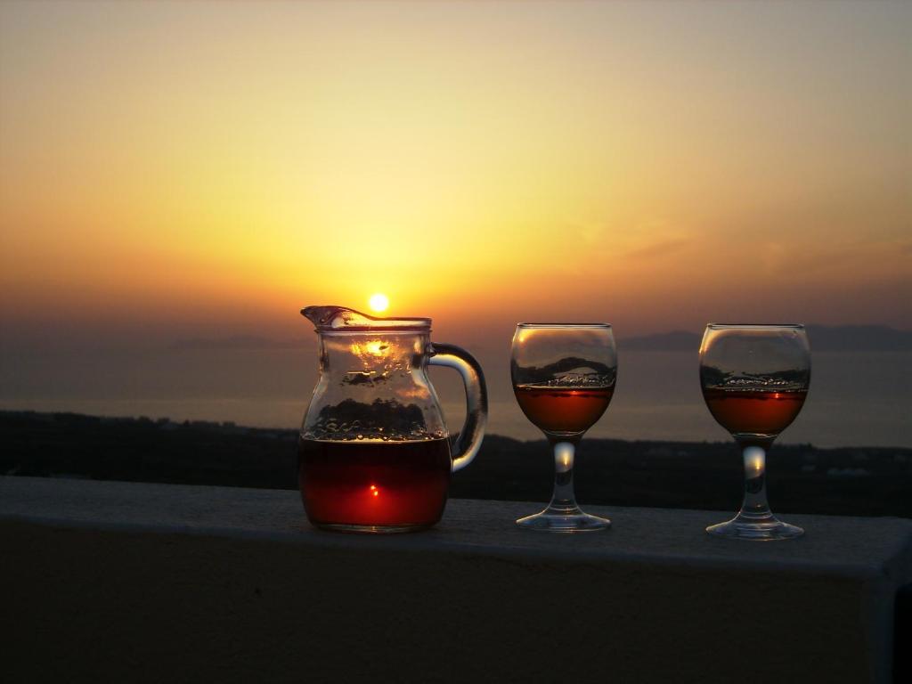 three glasses of wine and a vase with the sunset at Kiklamino Sunset Studios in Oia