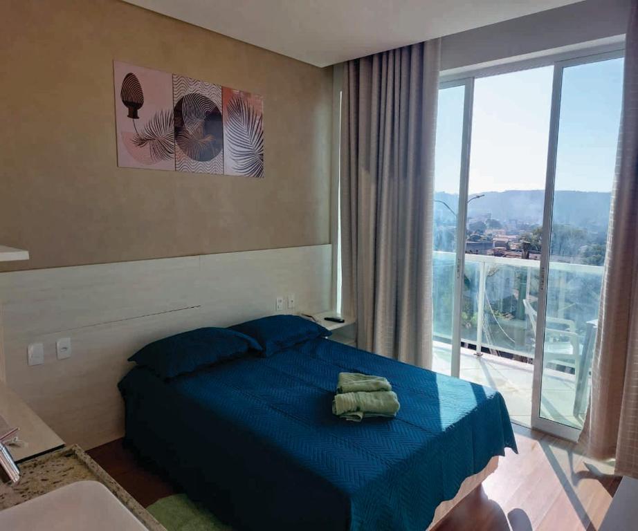 1 dormitorio con cama azul y ventana grande en Apto com varanda, self check-in, ar, TV e 14km aeroporto, en Lagoa Santa