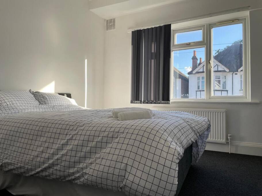 ein Schlafzimmer mit einem Bett mit einer Decke und einem Fenster in der Unterkunft 4 Bed: 5mins frm Wembley Stadium in London
