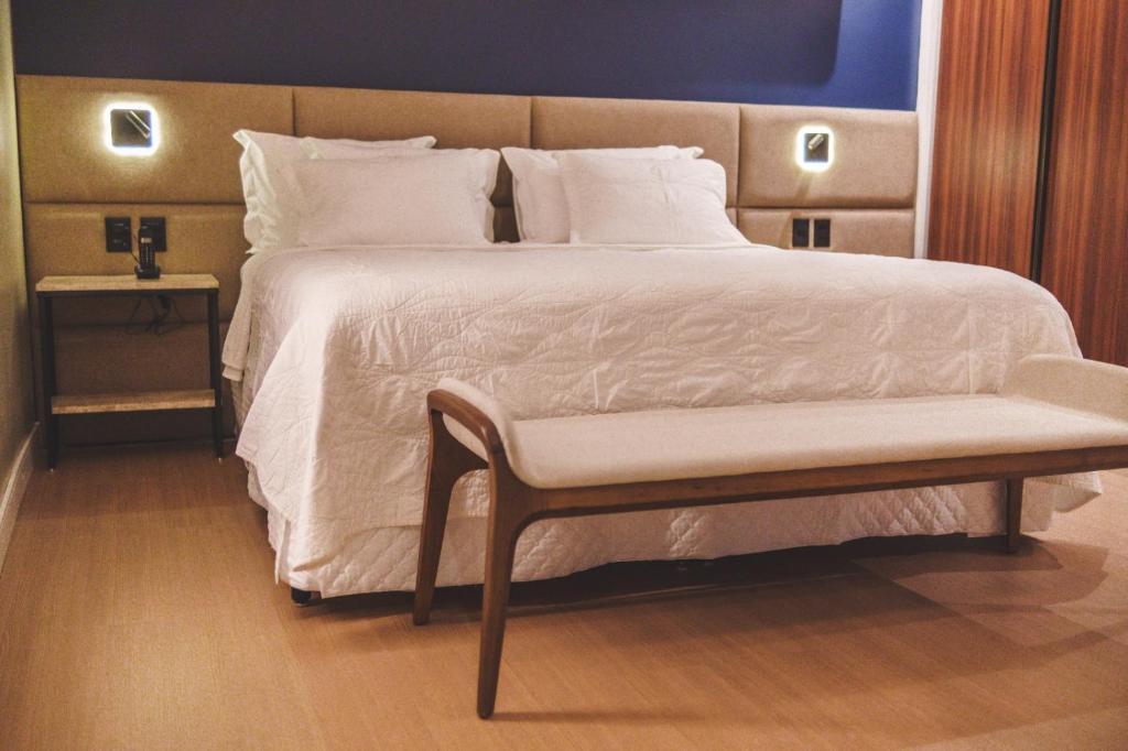 a bedroom with a large bed with a bench next to it at Hotel Serrano in Campina Grande