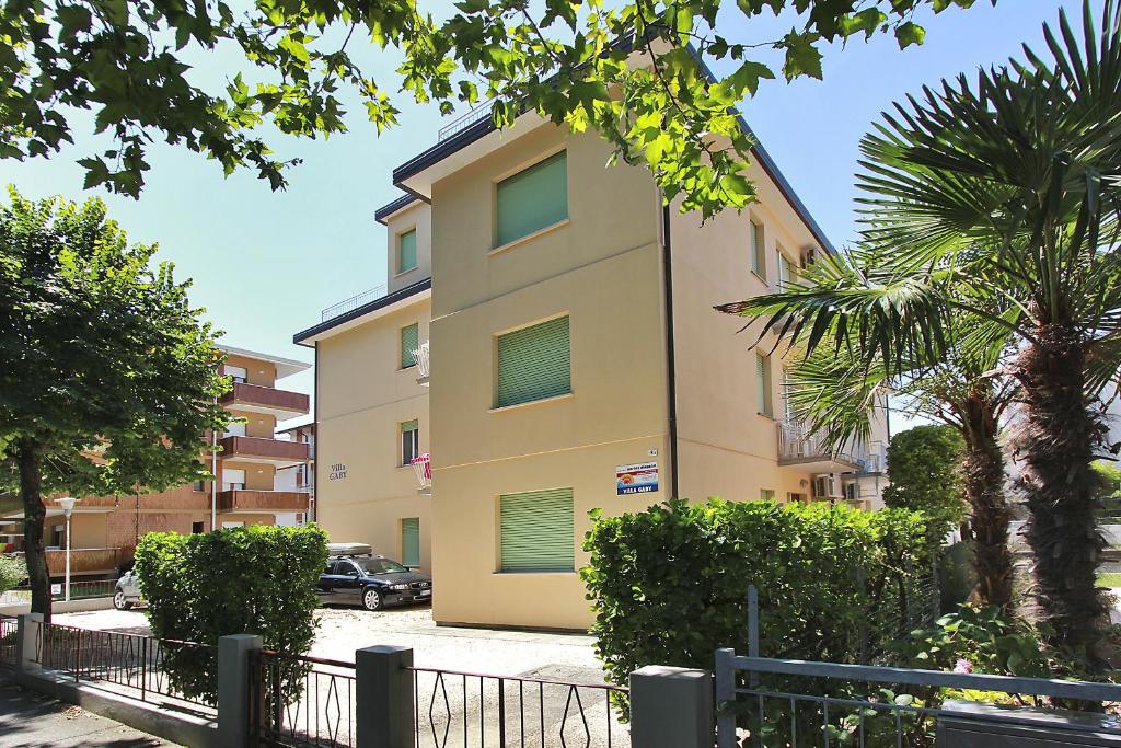 un edificio alto de color amarillo con ventanas con contraventanas verdes en Appartamenti Gaby, en Lignano Sabbiadoro