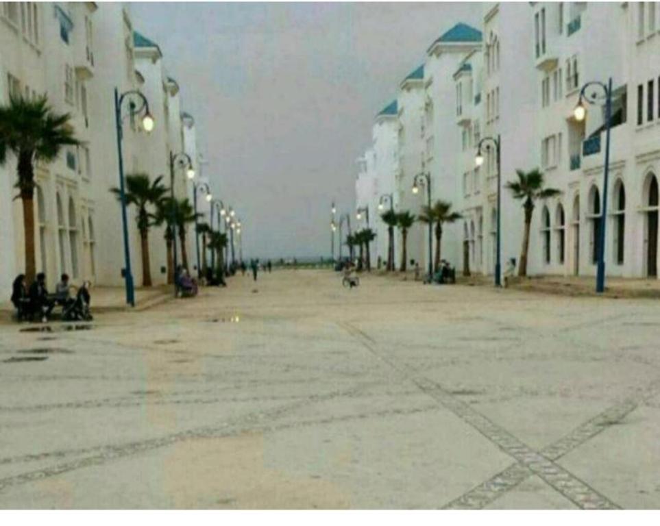 une rue vide avec des palmiers et des bâtiments dans l'établissement Massira 1, à Fnideq