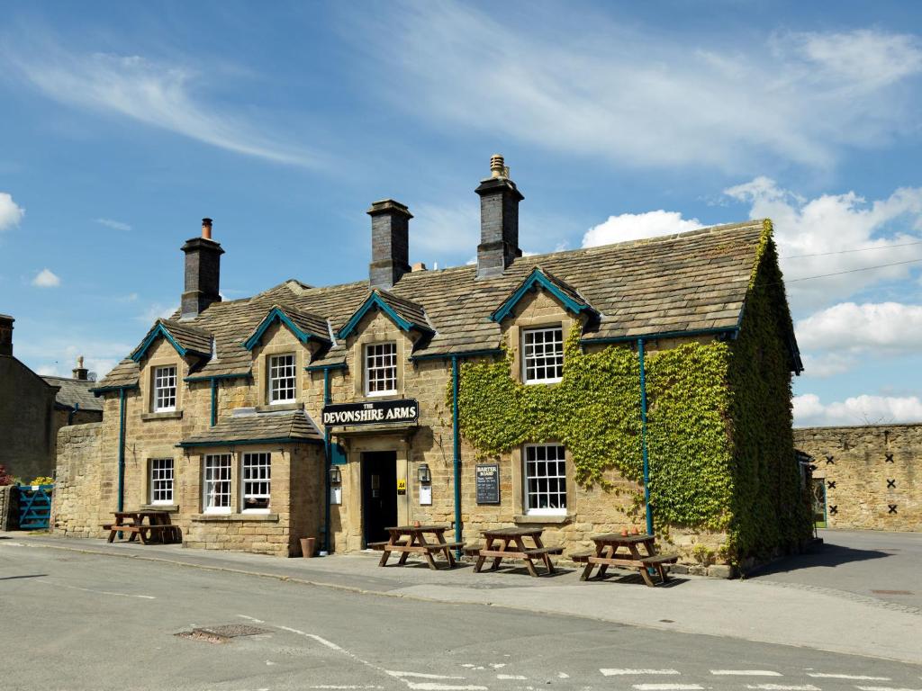 an old stone building with benches in front of it at Devonshire Arms at Pilsley - Chatsworth in Baslow