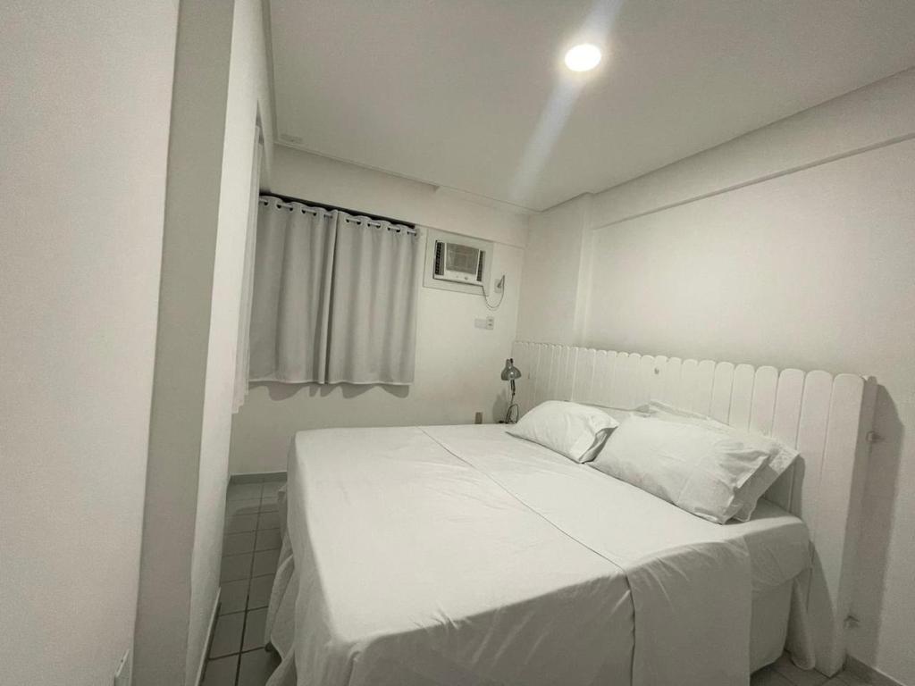 Cette petite chambre dispose d'un lit blanc et d'une fenêtre. dans l'établissement BOA VIAGEM 2 quartos 100 m da praia até 5 pessoas, à Récife