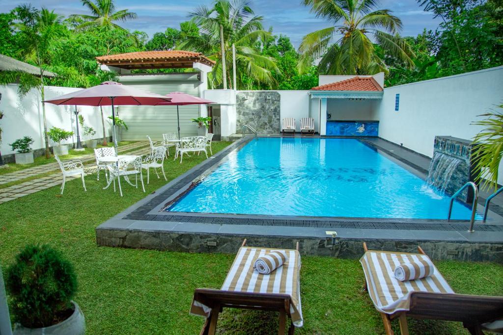 a pool with chairs and umbrellas next to a house at Superresidence in Balapitiya