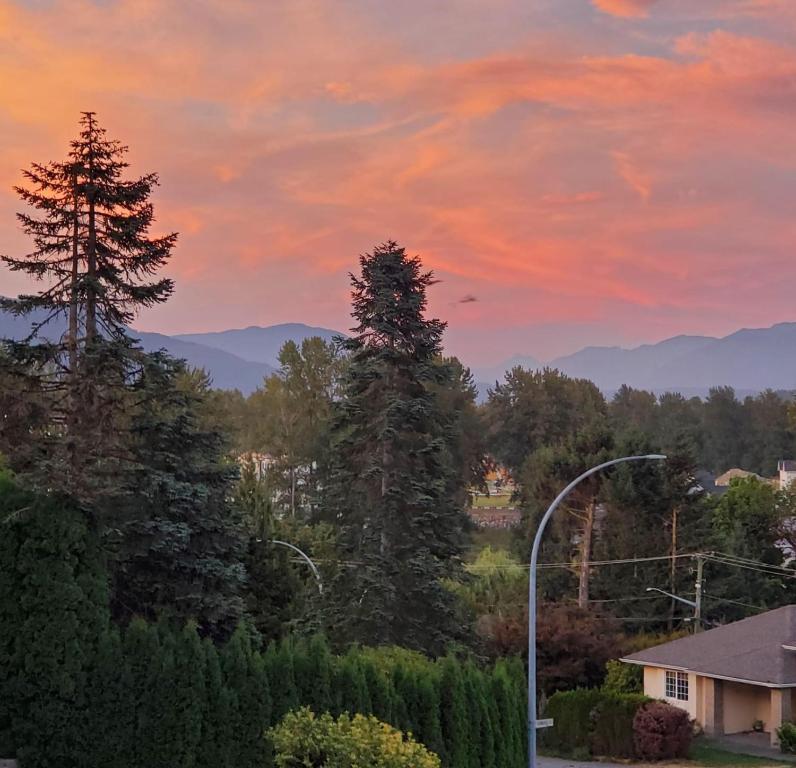 Blick auf den Sonnenuntergang mit Bäumen und einem Haus in der Unterkunft Licensed Mountain Retreat Garden House Near Heritage Park, Cultus Lake in Chilliwack