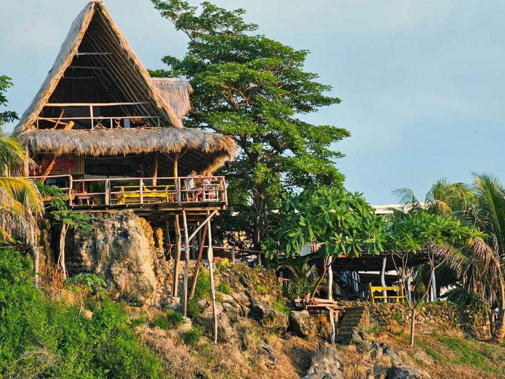 a resort with a thatched roof on a cliff at Monkey House Hostel in Tola