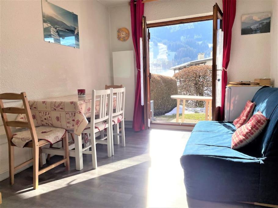 un salon avec un canapé, une table et une fenêtre dans l'établissement Charmant studio + jardin vue pistes et local velo, à Praz-sur-Arly