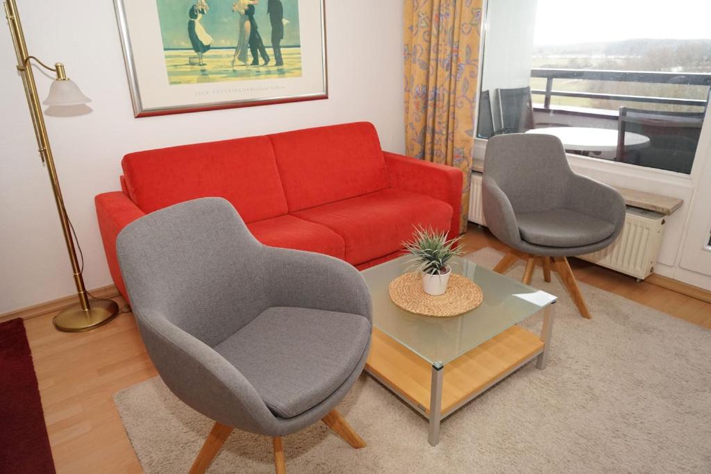 een woonkamer met een rode bank en 2 stoelen bij Penthousewohnung vor der Promenade in Damp