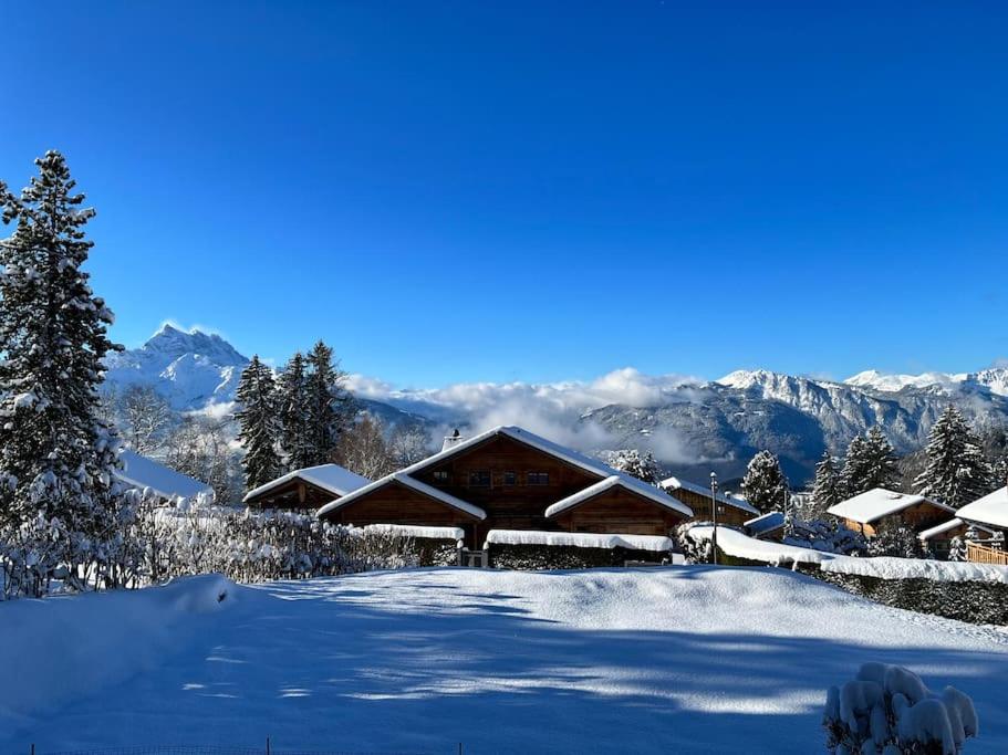 a log cabin covered in snow with mountains in the background at Appartement - Villars Sur Ollon in Villars-sur-Ollon