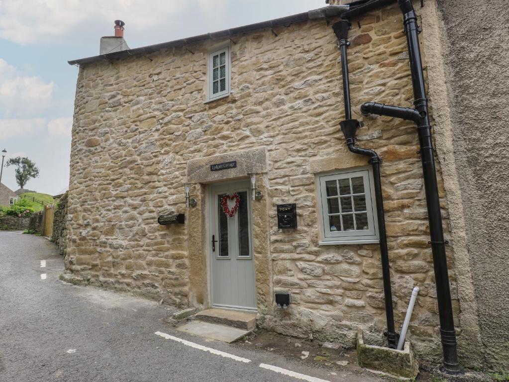 an old stone building with a white door at Lydgate Cottage in Eyam