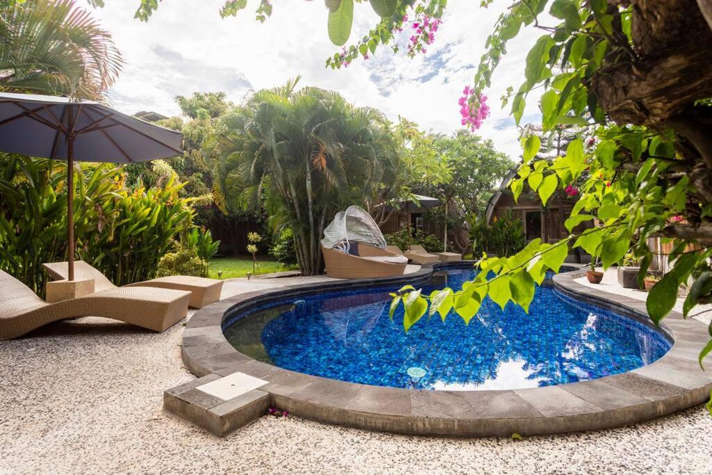 a swimming pool in a garden with an umbrella at Djamezz Lumbung in Gili Islands
