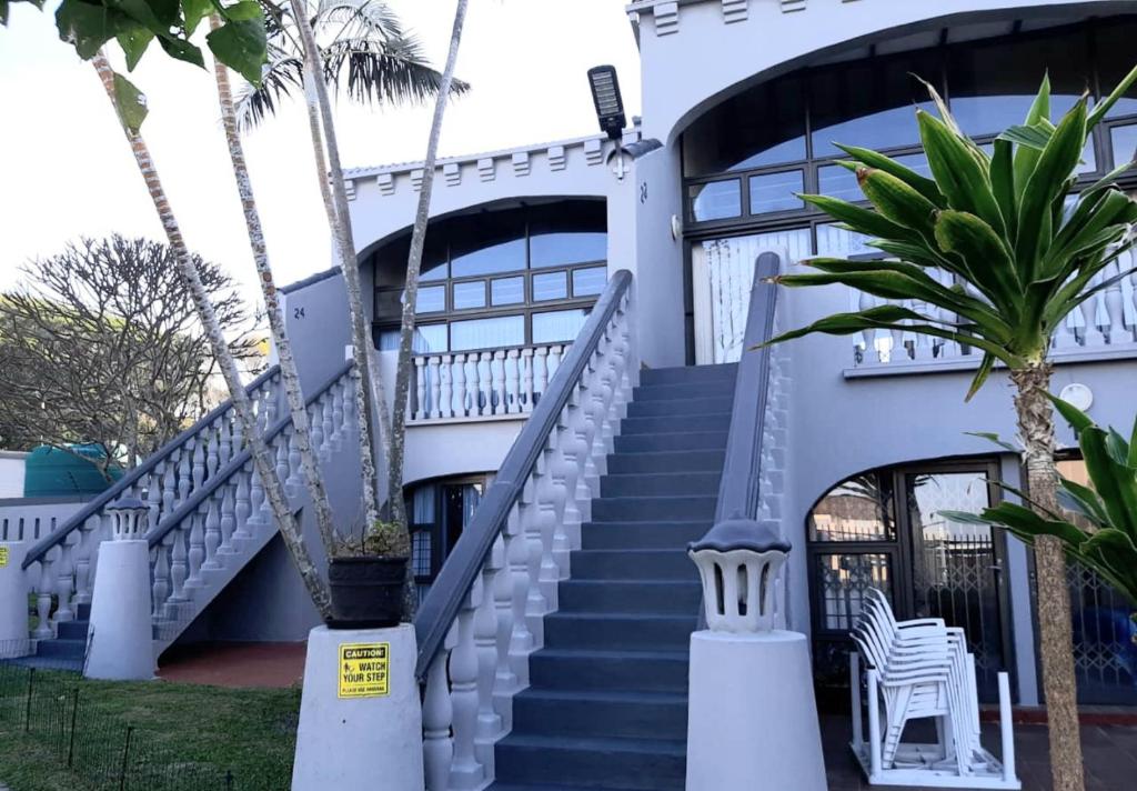 a white building with stairs and a palm tree at Uvongo cabanas in Margate
