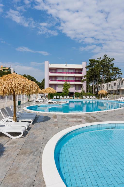 a pool with chairs and umbrellas in front of a building at Ducale in Bibione