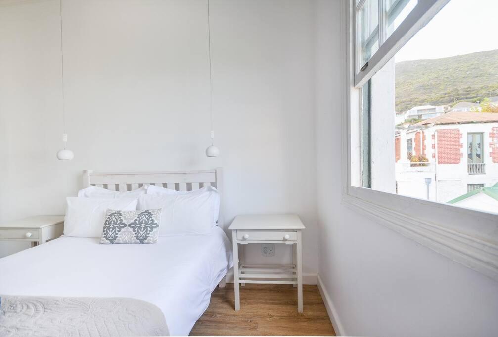 a white bedroom with a bed and a window at Sunny Windsor Apartment in Kalk Bay in Cape Town