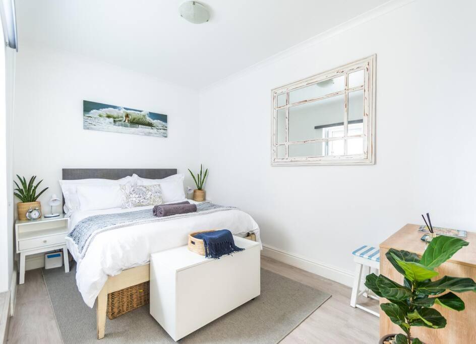 a white bedroom with a bed and a window at Dalebrook Cottage in the heart of Kalk Bay in Cape Town