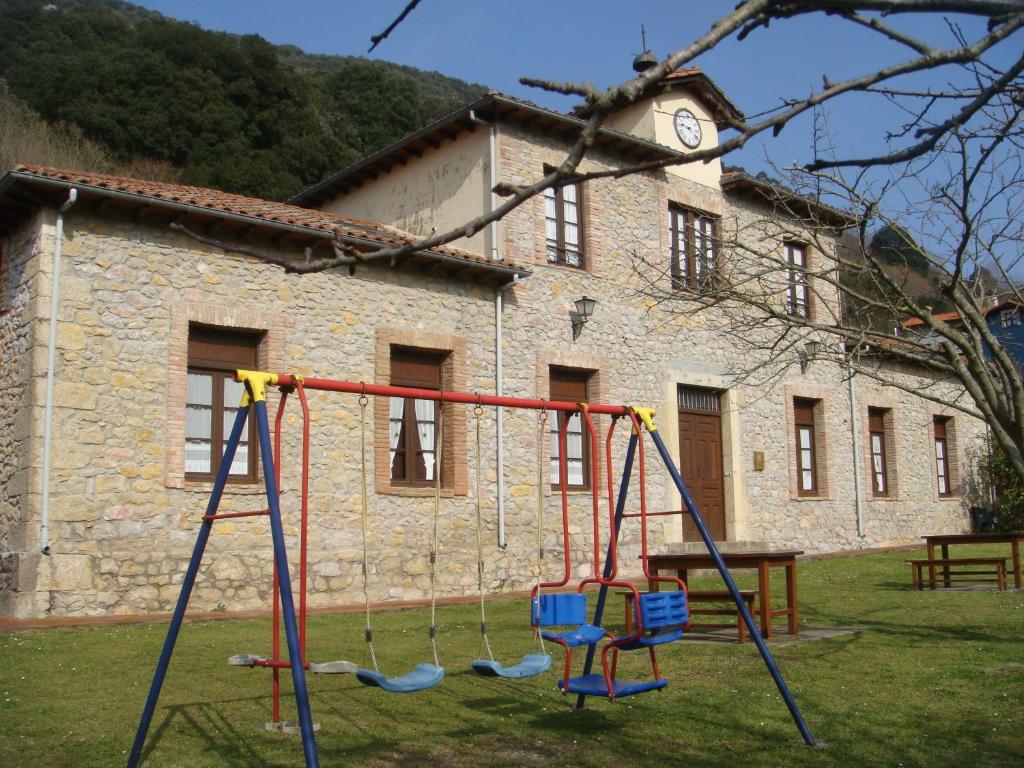 a playground in front of a stone building with a clock at Apartamentos Rurales La Escuela in Buelles