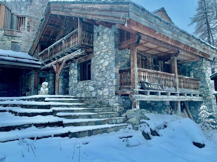 a stone house with a wooden deck and stairs in the snow at Chalet NANOUK in Le Joseray