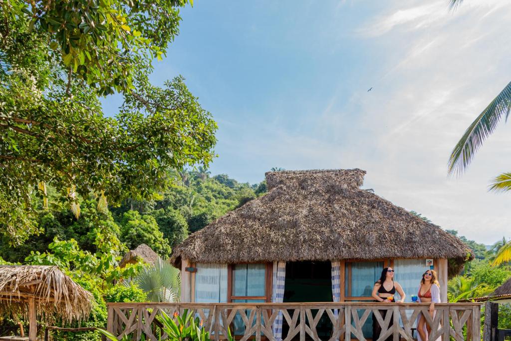 Duas mulheres em cima de uma cerca de madeira em frente a uma cabana. em Amaca Beach Hotel - Eco Resort Quiimixto em Quimixto