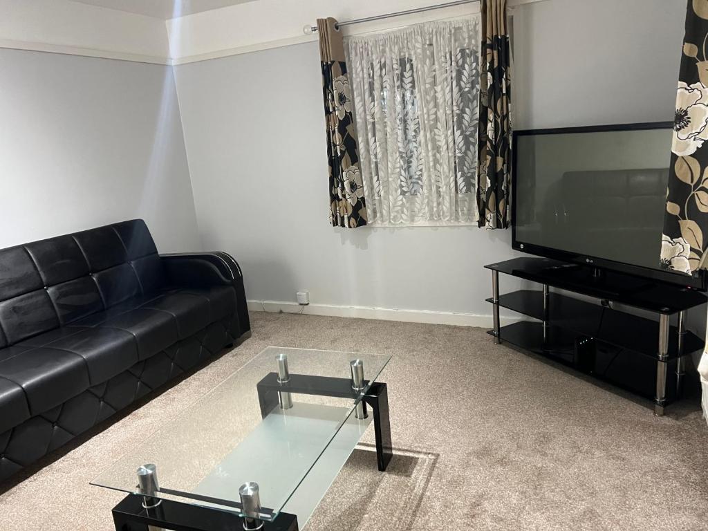 a living room with a black couch and a flat screen tv at Cosy 2 bedroom flat in London
