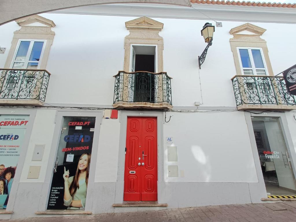 a white building with a red door and a balcony at Albergaria Formosa in Faro